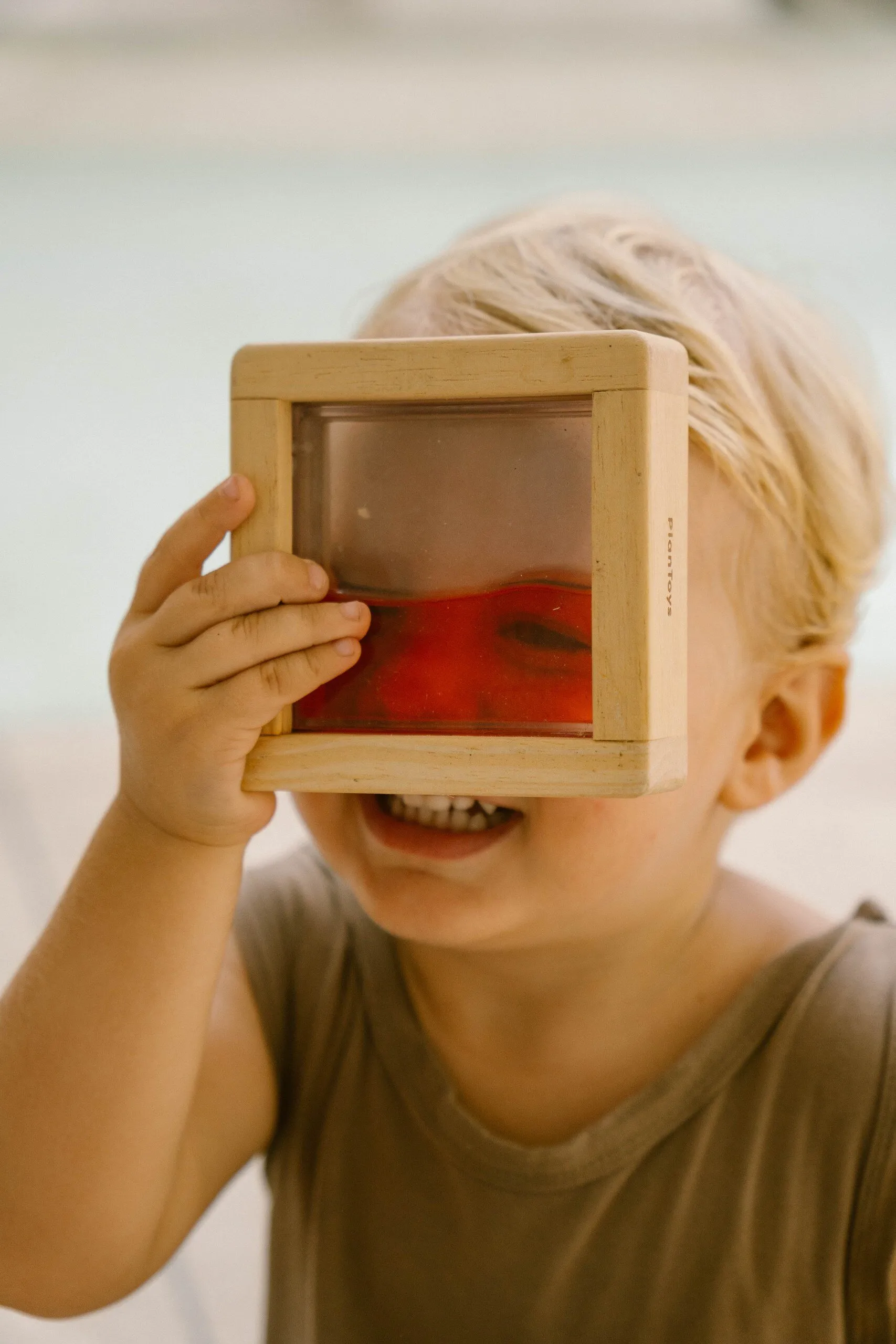 A smiling child looking through a wooden frame of coloured water